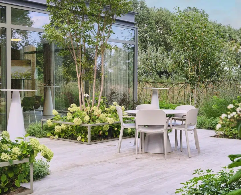 Groen terras bij een kantoorgebouw met tafel, stoelen en weelderige beplanting
